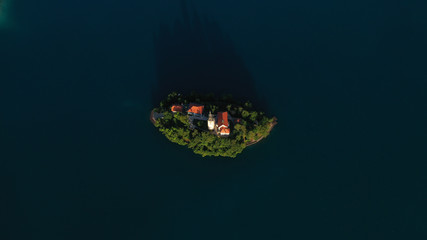 Fototapeta na wymiar Aerial view of small island with Church of assumption of Mary in the middle of Lake Bled, Slovenia. Summer. Green Mountains landscape around lake.