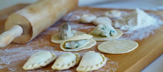 On the kitchen cutting board, ready-made dumplings with ingredients for making dough and various kitchen utensils.
