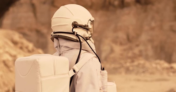 Female NASA astroaut wearing a full equipped space costume and walking at the Mars, then looking at the camera. Outdoor.
