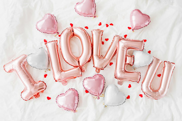 Pastel pink Air Balloons in the shape of the word "I LOVE U" with heart on bed. Love concept. Holiday, celebration. Valentine's Day or wedding/bachelorette party decoration. Foil balloon