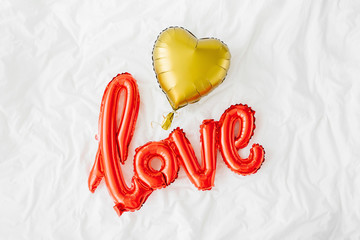Red Air Balloons in the shape of the word "Love" with golden hearts on bed. Love concept. Holiday, celebration. Valentine's Day or wedding/bachelorette party decoration. Foil balloon