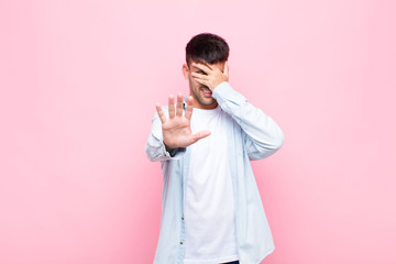 young handsome man covering face with hand and putting other hand up front to stop camera, refusing...