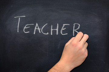 Teacher's hand writing the word teacher on a blackboard