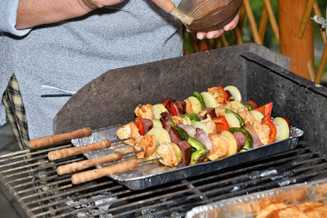 A human puts a spice sauce on meat and vegetables on the grill