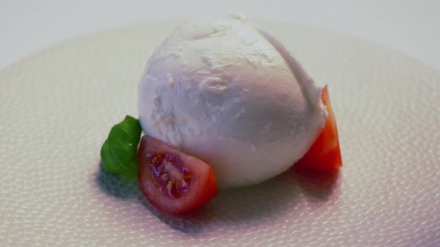 Soft white italian mozzarella cheese rotating on white plate
