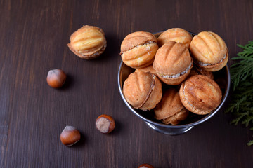 Walnut shaped shortbread cookies with cream filling in a metal cup against the dark background