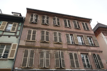 Facade or façade of a historical residential house in Colmar, Alsace, France. The windows have shutters, some of them are closed. the facade is stained by water and time.