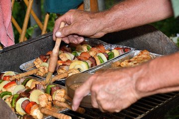 A human puts a spice sauce on meat and vegetables on the grill