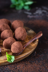 Dark chocolate truffles candy with raw cocoa powder and mint in a wooden bowl, dark brown stone background. 