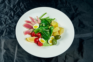 Close up view on tasty Appetizing salad with fresh medium-rare grilled tuna, capers, cherry tomatoes, asparagus on a white plate on a black background