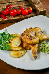 Close up view on tasty baked half of chicken with roasted potato on white plate on wooden background