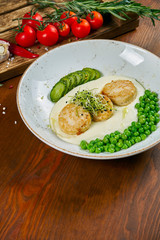 Fried chicken meatballs (cutlets) garnished with peas, mashed potatoes and cucumber in a white bowl on a wooden background. Tasty and healthy diet food. Close up view.