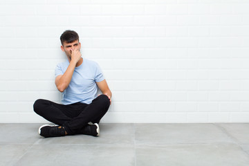 young handsome man feeling disgusted, holding nose to avoid smelling a foul and unpleasant stench...