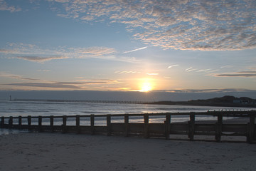 Obraz premium Beautiful Sunset on Littlehampton seafront as the sun dips behind cloud on the horizon, reflecting vibrant colours onto the clouds.