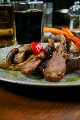Juicy rack of a young lamb with vegetables and green pasta on a white plate. Restaurant serve from the chef. Wooden background. Close up, selective focus. Food flat lay