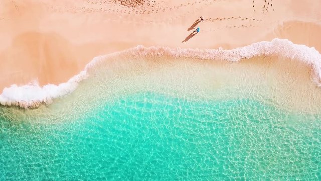Couple walk along the perfect tropical beach with calm rolling waves