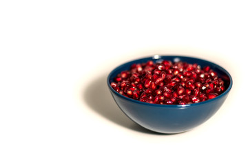 blue plate full of pomegranate seeds on a white background, isolate, side view