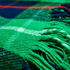 Structure of the fabric of a wool blanket with tartan plaid in green color, close-up, macro with selective blur in the background