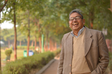 Happy senior Indian man wearing a suit standing and laughing in a park wearing tweed coat in...