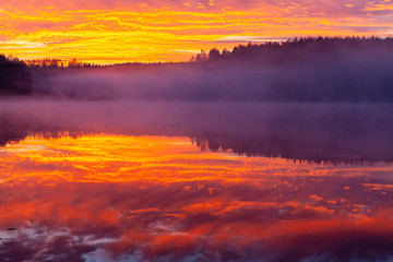 Incredibly red clouds on the sky looking like in fire, reflected in Ozierany lake, Poland.