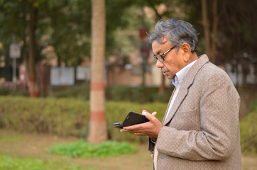 Obraz premium Lifestyle shot of senior Indian man wearing a tweed coat working on a phone in a park in New Delhi, India Concept - Digital India and digitally literate citizens 