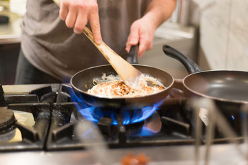 Cooking pasta on high heat. Cook hands are preparing sauced pasta in a kitchen