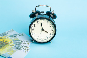 Time and money concept. Euro cash and alarm clock on a blue background