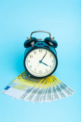Time and money concept. Euro cash and alarm clock on a blue background