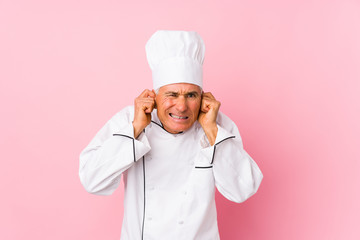 Middle aged cook man isolated covering ears with hands.
