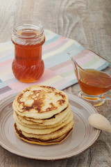 A large stack of steaming pancakes on a white plate with syrup being poured and dripping down the sides on a golden brown background