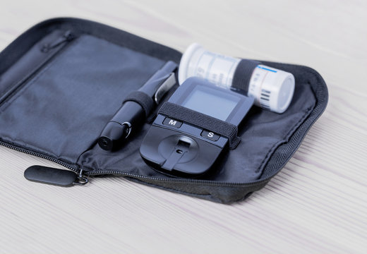 Glucometer, lanset and test strip lies in bag case on the wooden table on the left side. Concept of health, medicine.