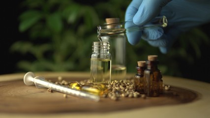 Filling up glass jar bottle with cannabis cbd oil mixture for oral medical use. Made of green...