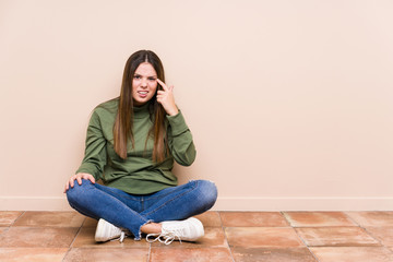 Young caucasian woman sitting on the floor isolated showing a disappointment gesture with forefinger.