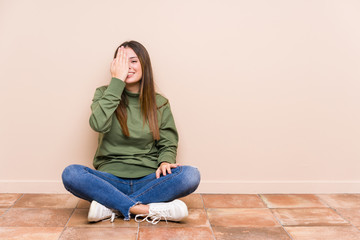 Young caucasian woman sitting on the floor isolated having fun covering half of face with palm.
