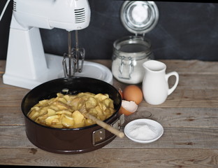 On the kitchen cutting board baking dish with dough. Ingredients and kitchen utensils nearby on an ancient wooden table.