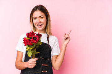 Young caucasian woman holding a roses isolated smiling cheerfully pointing with forefinger away.