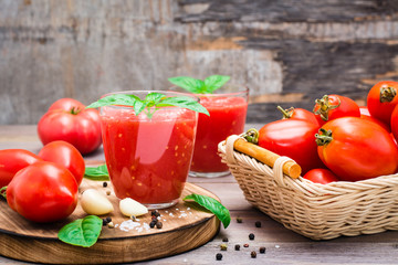 Blended fresh tomato juice with basil leaves in glasses and ingredients for its preparation on a wooden table