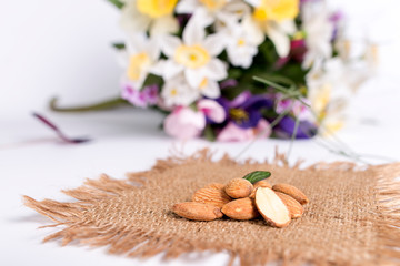 Close up of healthy and raw almonds placed on a rustic woven brown mat, decorated with green leaves, isolated on a white background