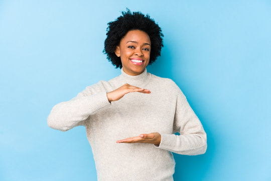 Middle aged african american woman against a blue background isolated holding something with both hands, product presentation.