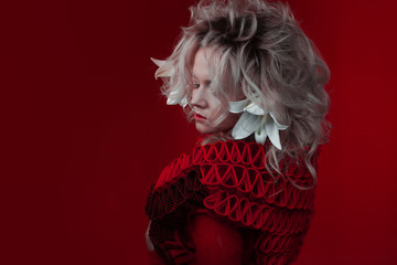 Shades of red. Strange attractive woman in a red outfit, on a red background, with lily flowers in...
