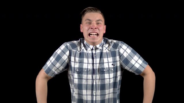 The young man is screaming. A man screams strongly in a shirt on a black background