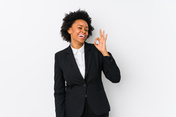 Middle aged african american business  woman against a white background isolated winks an eye and holds an okay gesture with hand.