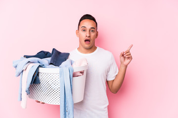Young latin man picking up dirty clothes isolated pointing to the side