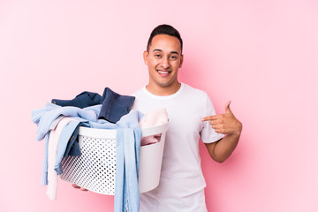 Young latin man picking up dirty clothes isolated person pointing by hand to a shirt copy space,...