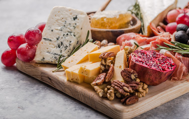 Traditional italian antipasto plate. Assorted cheeses on wooden cutting board. Brie cheese, cheddar slices, gogonzola, walnuts grapes, olives, prosciutto, rosemary and glass of red wine. top view