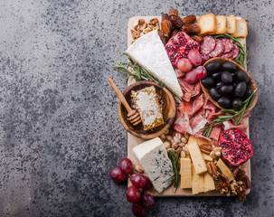 Traditional italian antipasto plate. Assorted cheeses on wooden cutting board. Brie cheese, cheddar slices, gogonzola, walnuts grapes, olives, prosciutto, rosemary and glass of red wine. top view