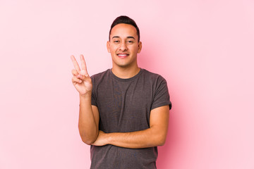 Yooung latin man posing in a pink backgroundshowing number two with fingers.