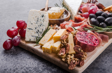 Traditional italian antipasto plate. Assorted cheeses on wooden cutting board. Brie cheese, cheddar slices, gogonzola, walnuts grapes, olives, prosciutto, rosemary and glass of red wine. top view