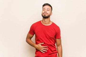 Young south-asian man touches tummy, smiles gently, eating and satisfaction concept.