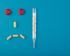 A medical thermometer and a sad smiley face made of pills. Space for text